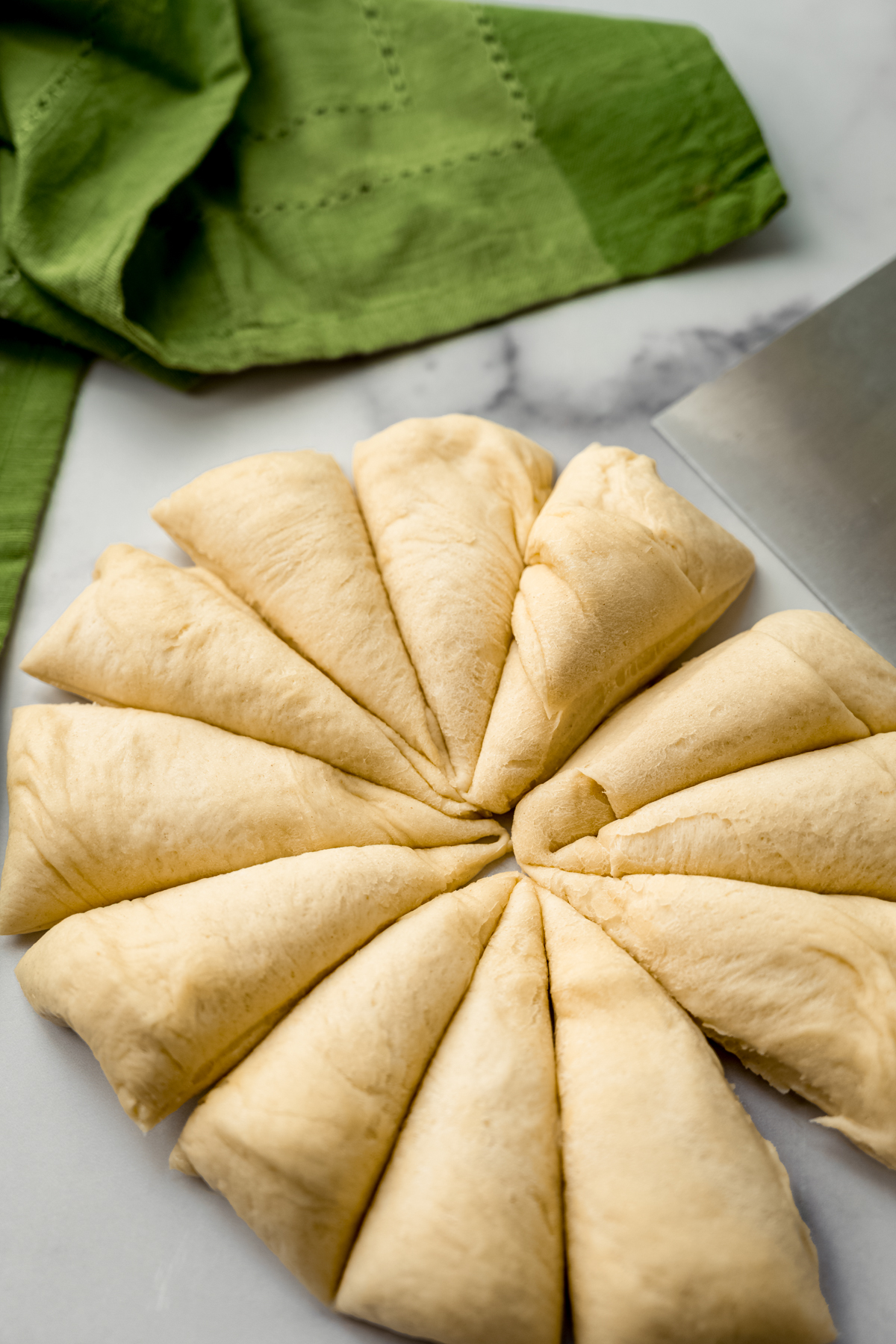 A circle of yeasted dough cut into 12 triangles with a bench scraper to make pull-apart bread.