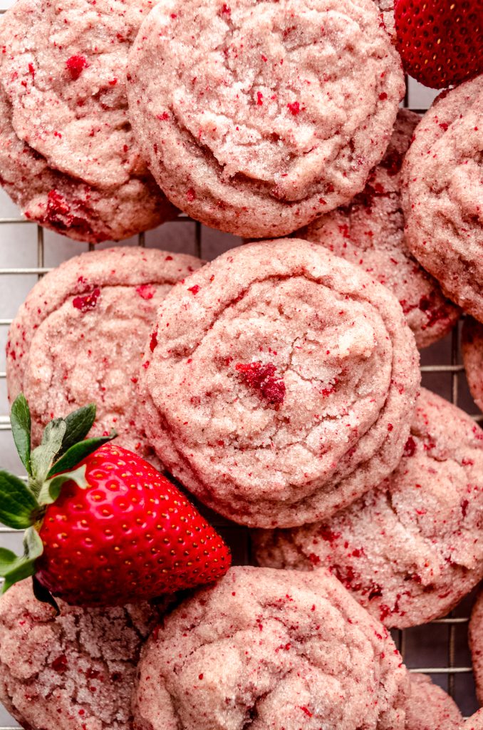 Aerial photo of strawberry sugar cookies on a cooling rack with fresh strawberries around them.