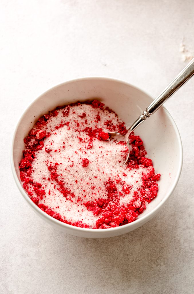 A bowl of granulated sugar with bits of freeze dried strawberries in it.