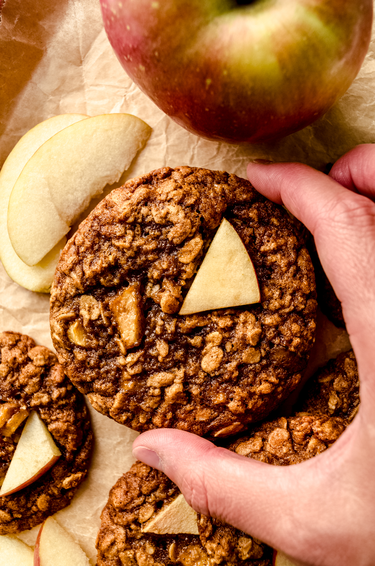 Someone's hand holding an apple oatmeal cookie on a surface.