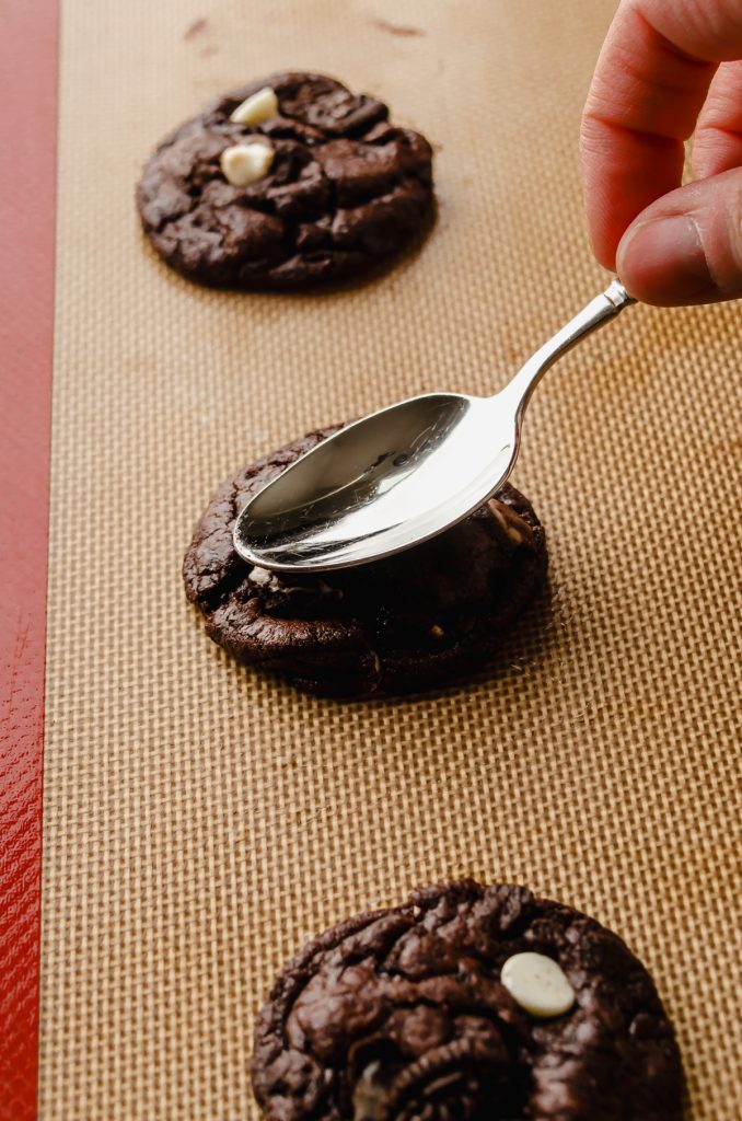 Someone is using a spoon to flatten a hot cookie.