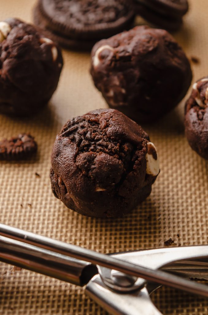 A chocolate cookies and cream cookie dough ball on a baking sheet.