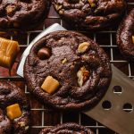 Someone is lifting a chocolate turtle cookie off of a cooling rack with a spatula.