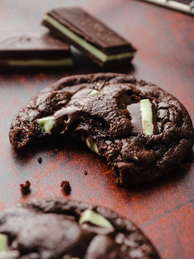 A mint chocolate cookie on a surface and a bite has been taken out of it.