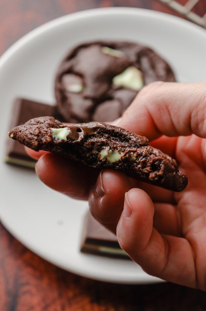 Someone is holding a mint chocolate cookie that has a bite taken out of it.