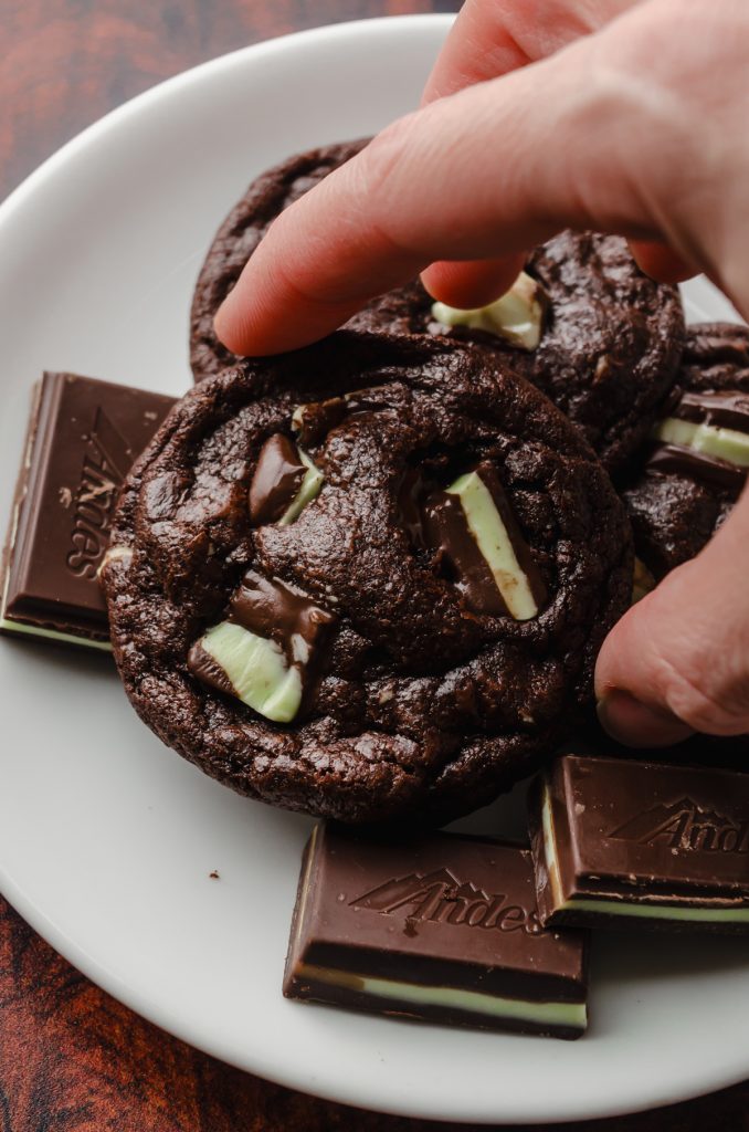 Someone is grabbing a mint chocolate cookie off of a plate of cookies.