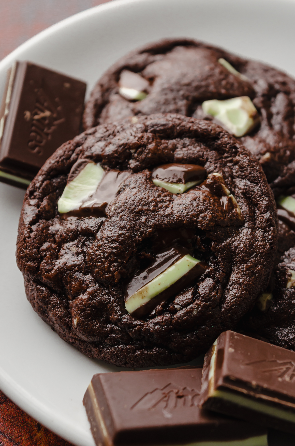 A chocolate mint cookie on a plate with Andes mints around it.