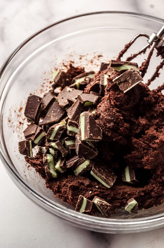 Chocolate mint cookie dough in a bowl with Andes mint pieces in it.