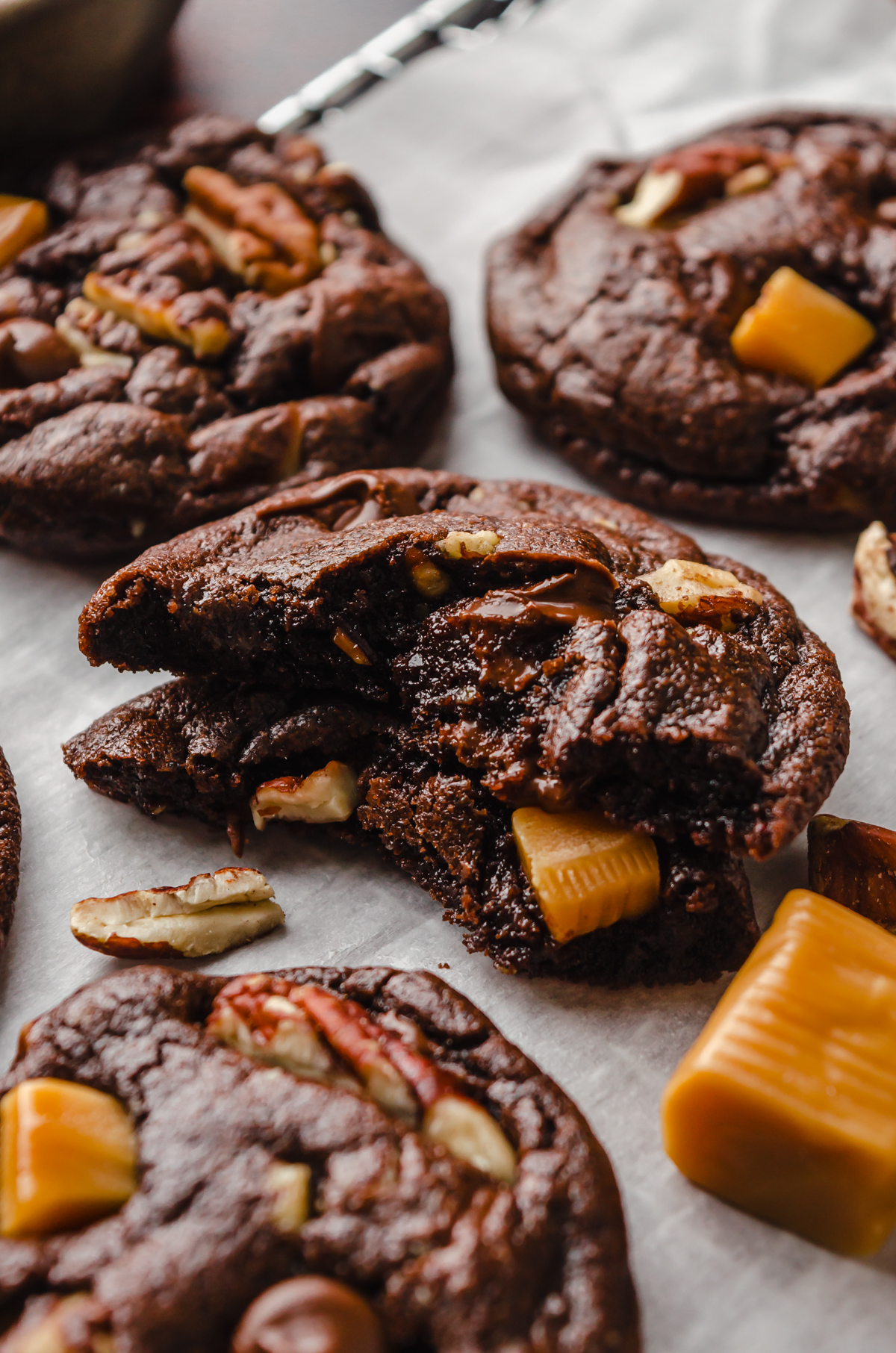 A chocolate turtle cookie that has been broken in half and sitting on a surface.