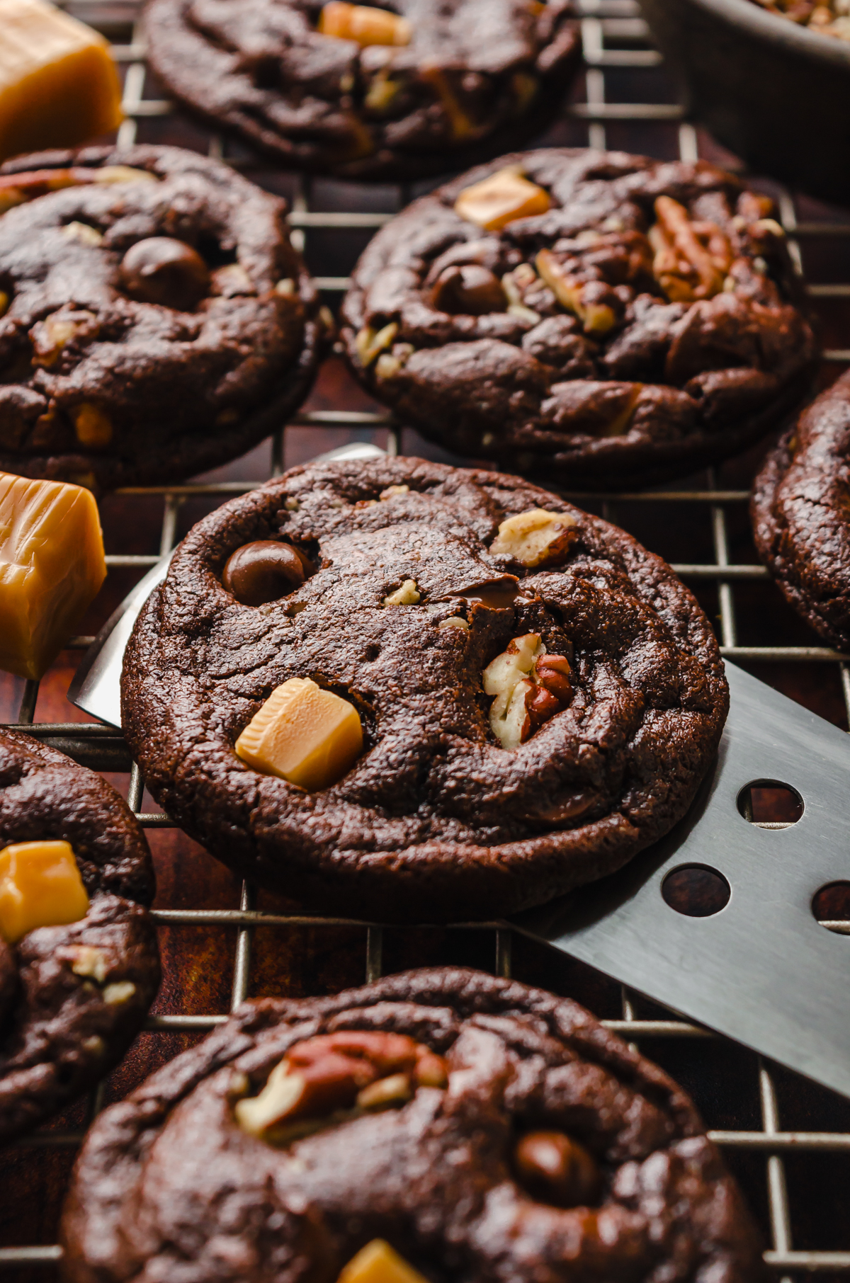 Someone is lifting a chocolate turtle cookie off of a cooling rack with a spatula.