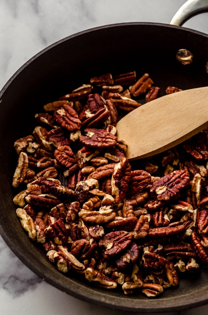 Pecans in a saucepan with a wooden spoon to toast them.