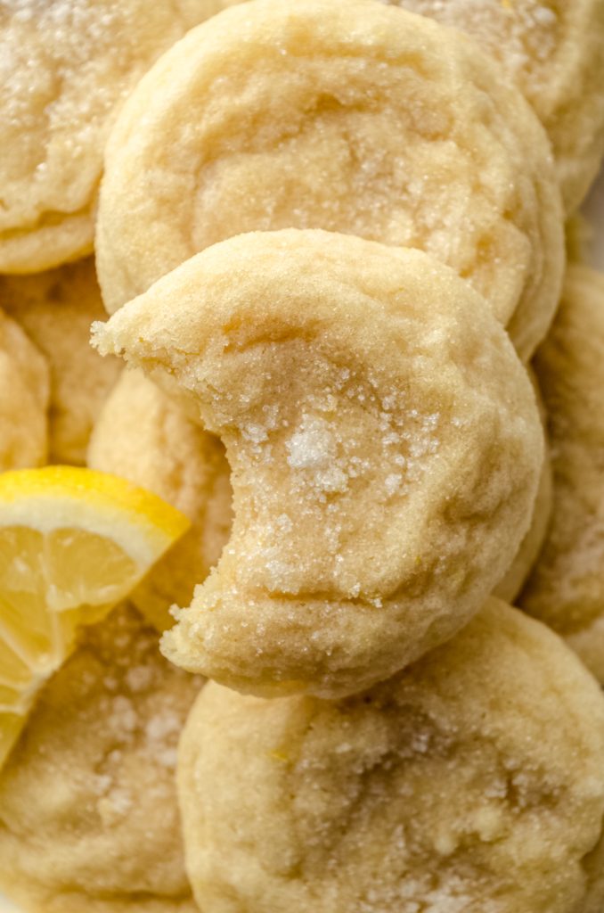 Aerial photo of a plate of lemon sugar cookies with lemon slices and a bite has been taken out of the one on the top.