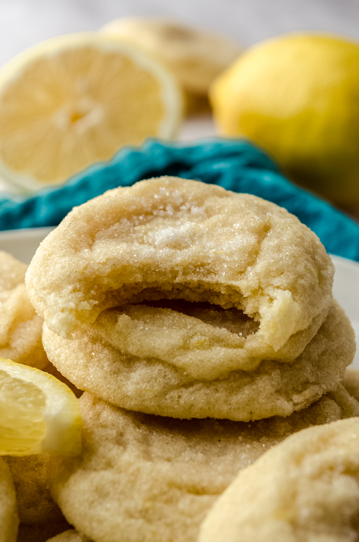 A plate of lemon sugar cookies with lemon slices and a bite has been taken out of one of them.