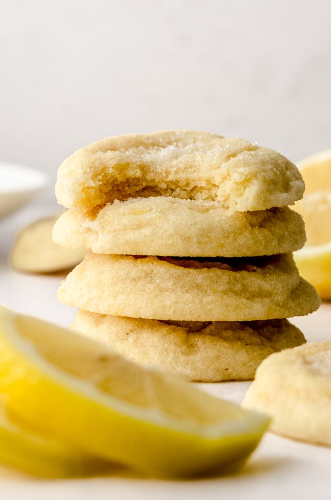 A stack of lemon sugar cookies with lemon slices and a bite has been taken out of the one on the top.