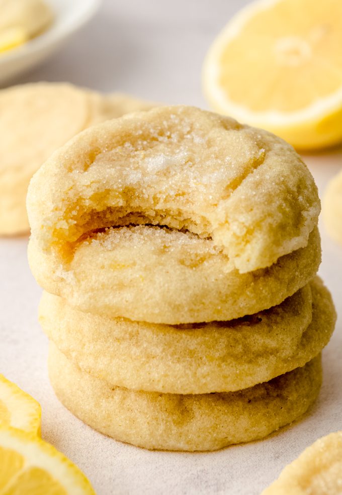 A stack of lemon sugar cookies with lemon slices and a bite has been taken out of the one on the top.