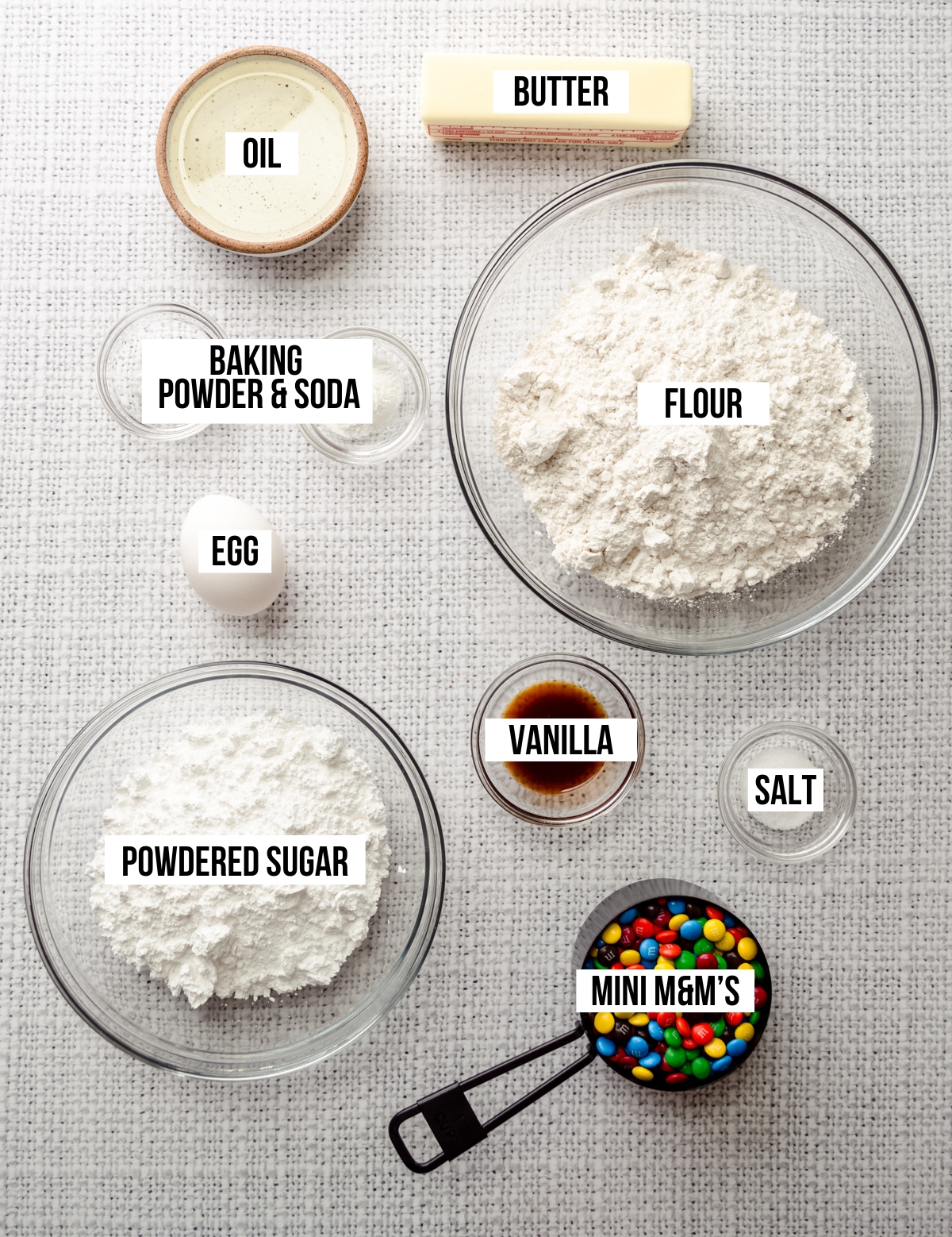 Aerial photo of ingredients to make m&m sugar cookies with text overlay labeling each ingredient.