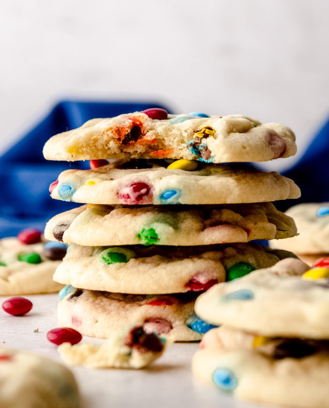 A stack of m&m cookies with a bite taken out of the one on the top.