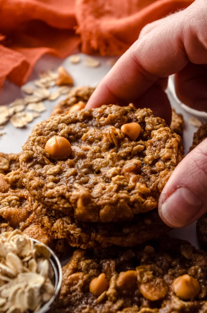 Someone is taking an oatmeal scotchie cookie off of the top of a pile of cookies.