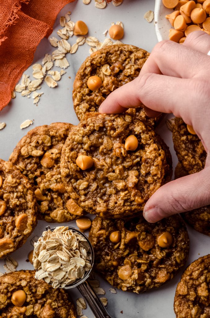 Aerial photo of someone holding an oatmeal scotchies on a surface with oats scattered around,