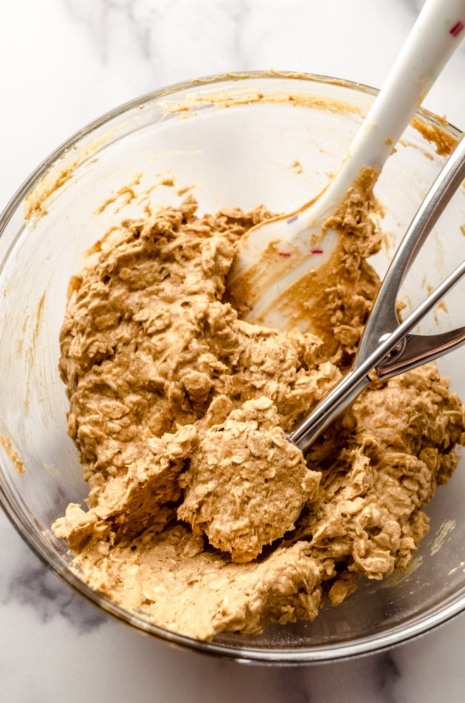 A bowl of oatmeal scotchies cookie dough with a cookie scoop in it.