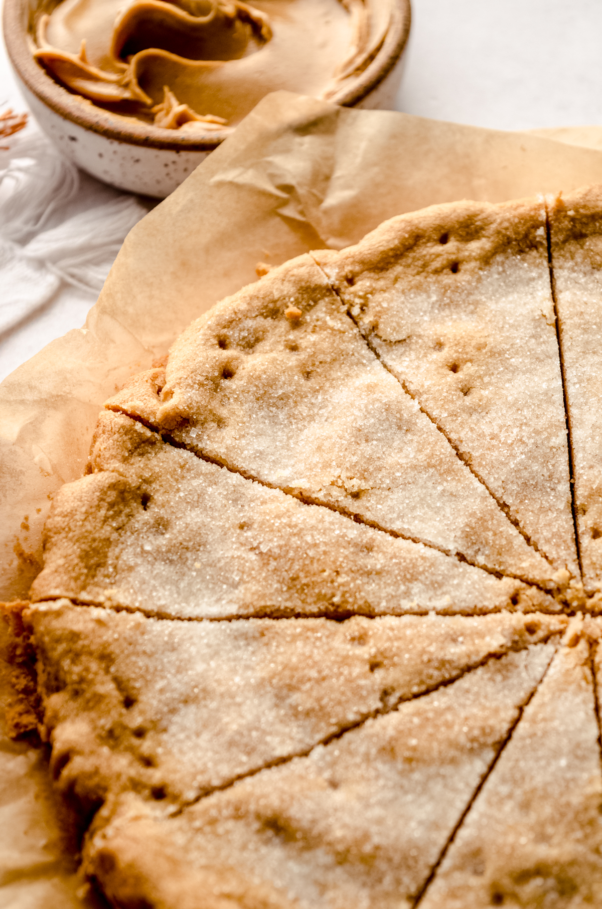 A circle of peanut butter shortbread sliced into pieces on a piece of parchment paper.