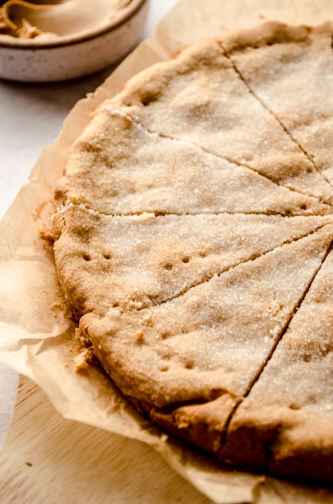 A circle of peanut butter shortbread sliced into pieces on a piece of parchment paper.