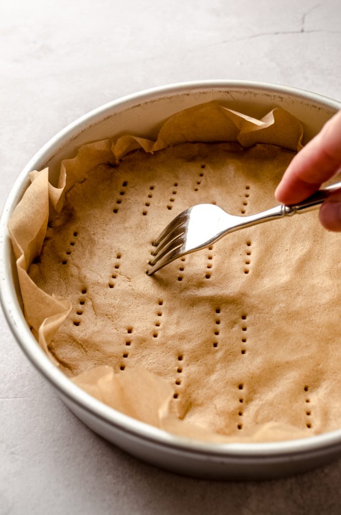 Someone is pricking peanut butter shortbread dough in a pan with a fork.