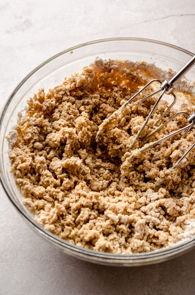 A bowl of peanut butter shortbread dough coming together with electric beaters in the bowl.