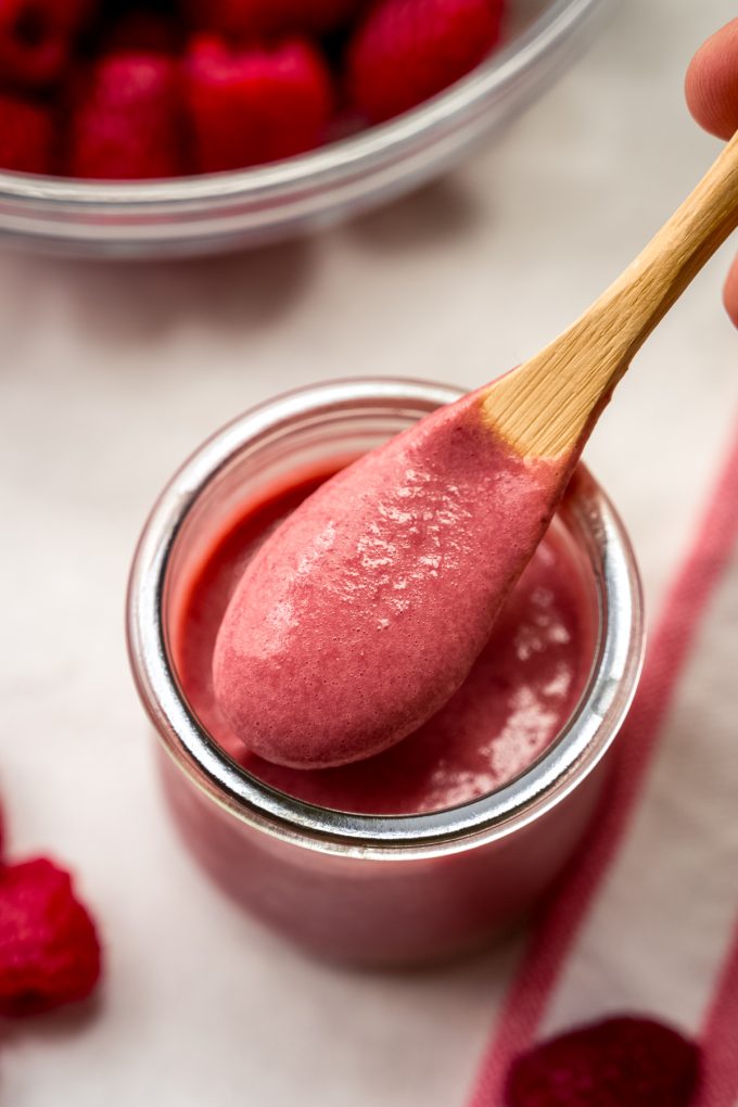 A spoonful of raspberry curd coming out of a jar.