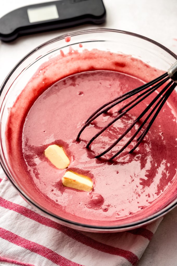 Someone is whisking butter into warm raspberry curd.