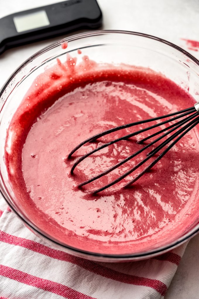 Someone is whisking raspberry curd in a large glass bowl.