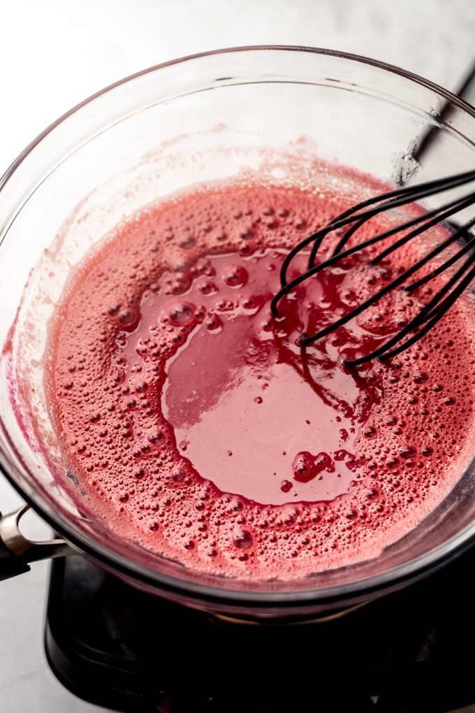 Someone is whisking raspberry curd over a double boiler.