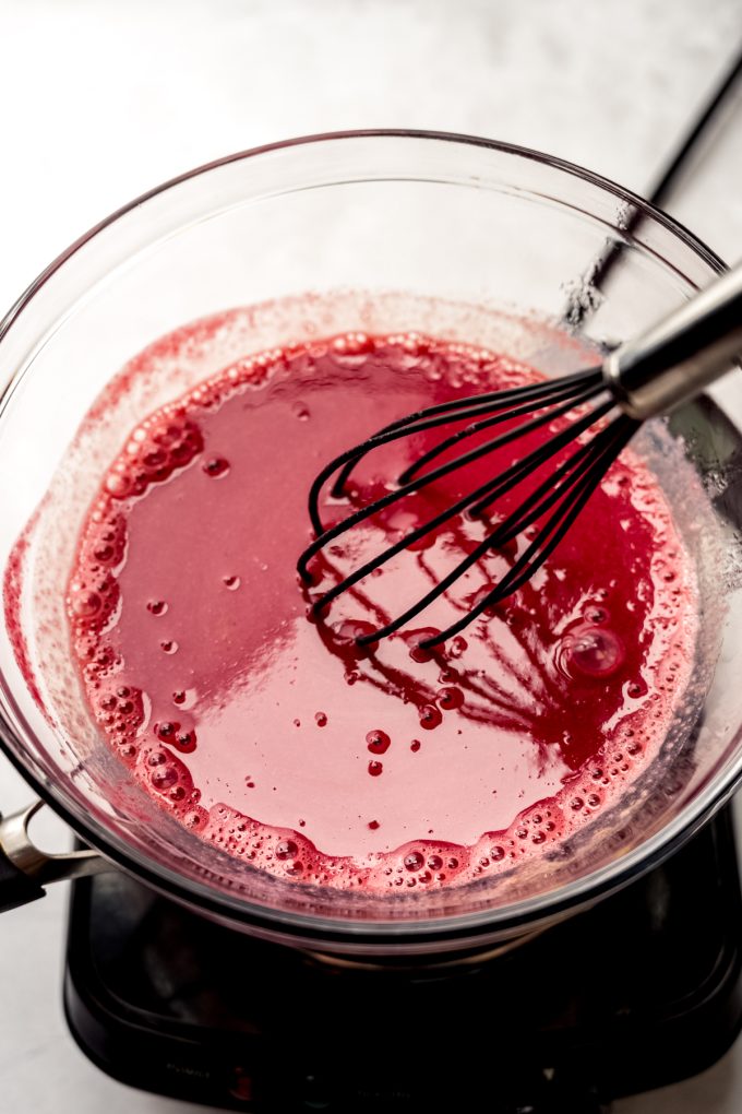 Someone is whisking raspberry curd over a double boiler.