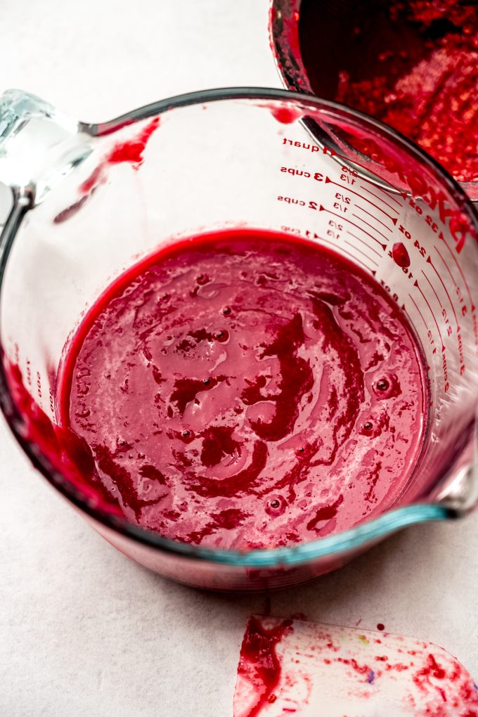 A large glass measuring cup filled with strained raspberry puree.