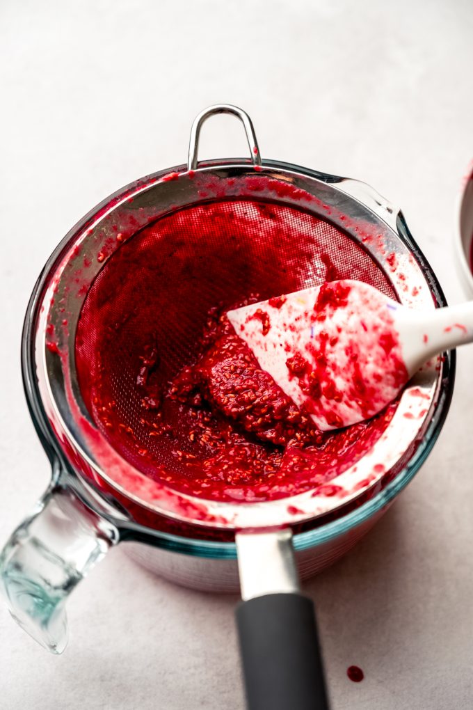Someone is pressing raspberry puree through a sieve with a spatula.