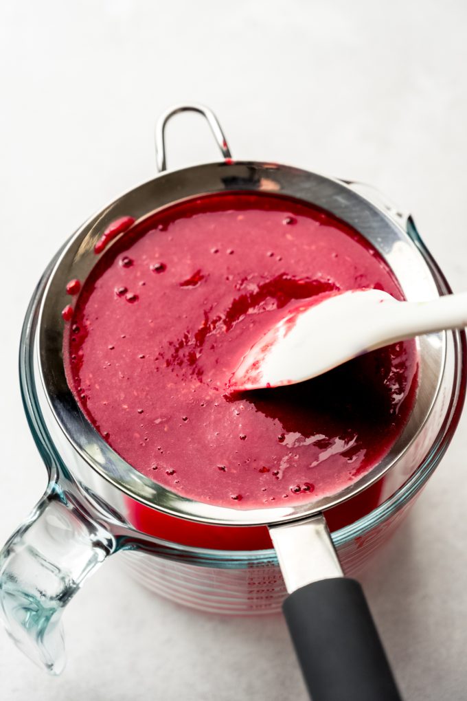 Someone is pressing raspberry puree through a sieve with a spatula.