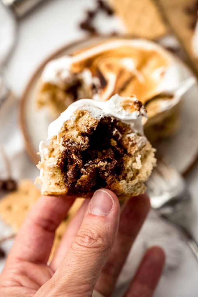 Someone is holding the center of a s'mores cinnamon roll in their fingers.