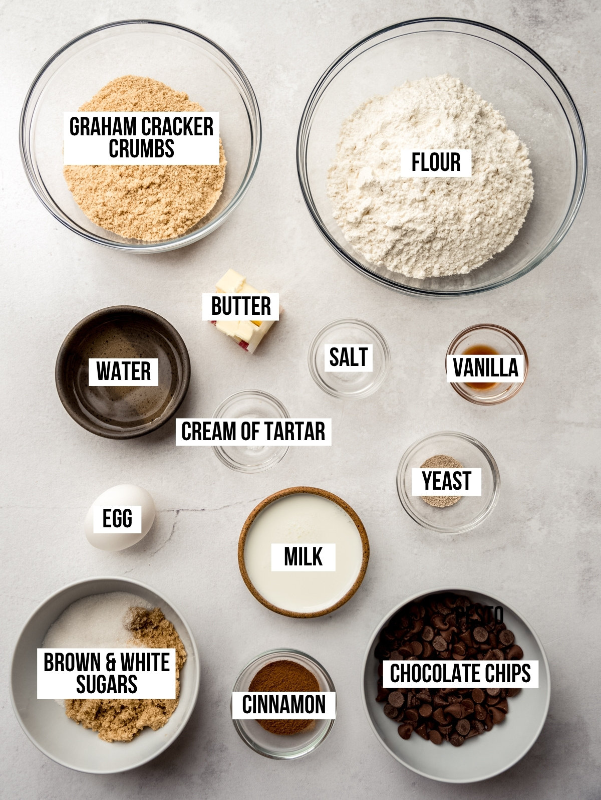 Aerial photo of ingredients to make s'mores cinnamon rolls on a surface and text overlay labeling each ingredient.