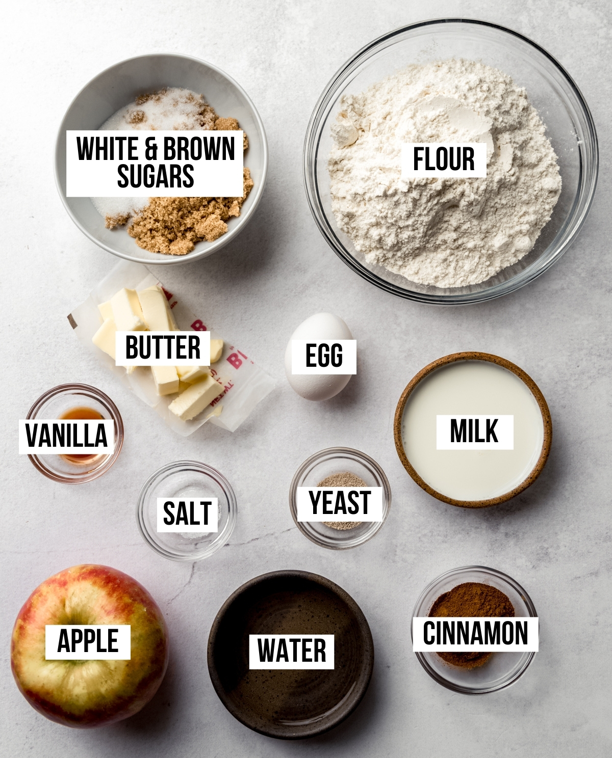 Aerial photo of the ingredients to make apple cinnamon rolls with text overlay labeling each ingredient.