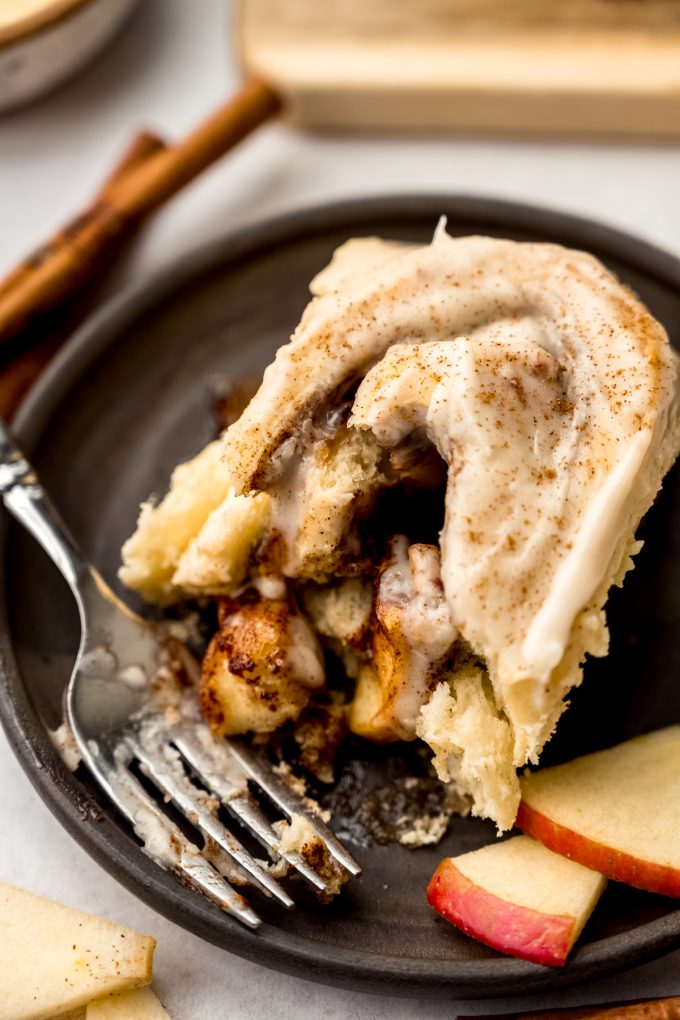 Aerial photo of an apple cinnamon roll on a plate with a fork and a bite taken out of the roll.