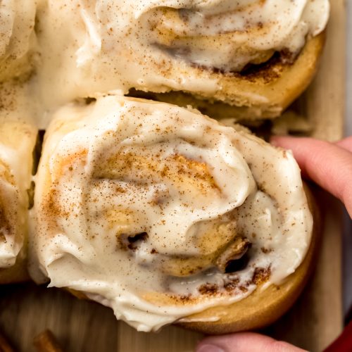 Aerial photo of someone's hand grabbing an apple cinnamon roll from a surface.