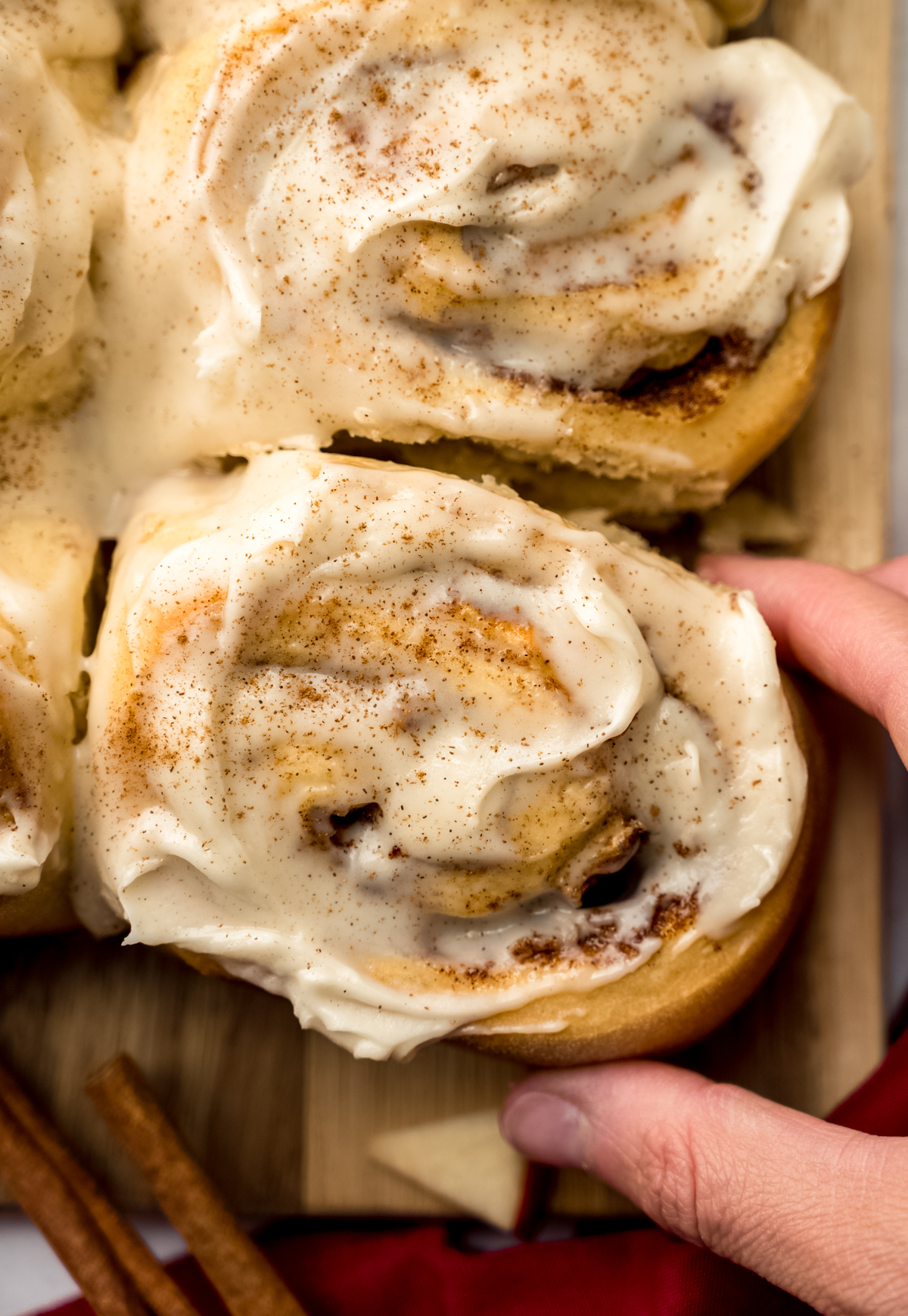 Aerial photo of someone's hand grabbing an apple cinnamon roll from a surface.