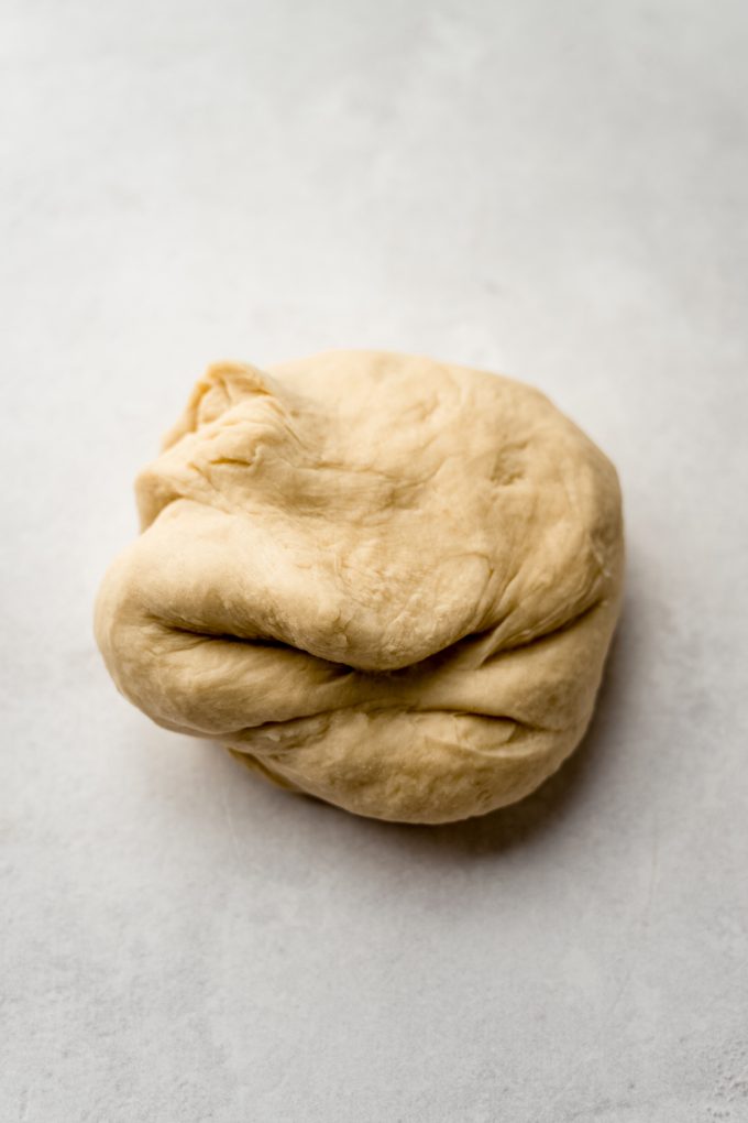 A ball of smooth yeasted cinnamon roll dough on s surface.