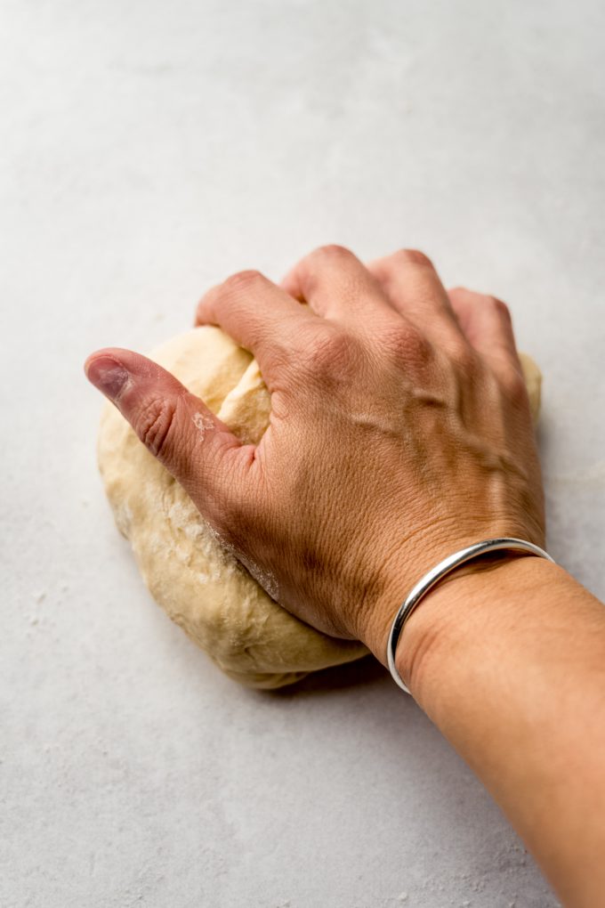 Someone's hand kneading yeasted cinnamon roll dough on a surface.