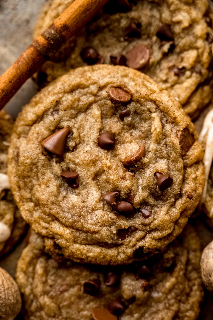 Aerial photo of spiced chocolate chip cookies on a surface with whole nutmeg and cinnamon sticks around it.
