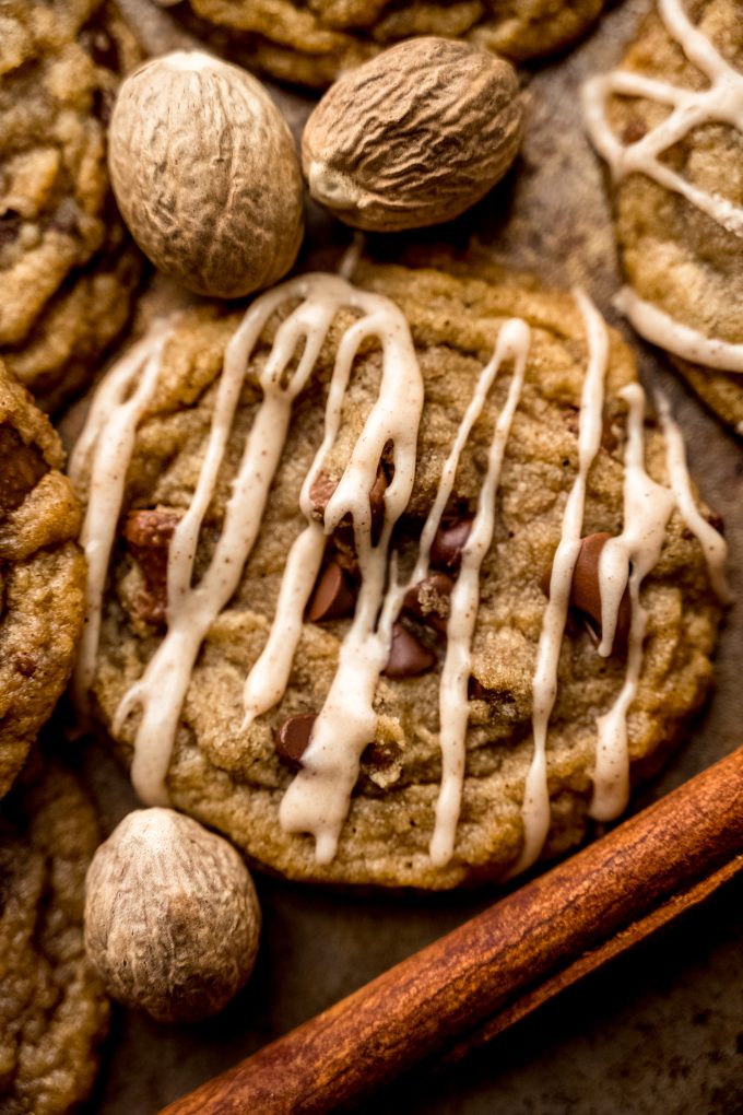 Aerial photo of spiced chocolate chip cookies on a surface with whole nutmeg and cinnamon sticks around it.