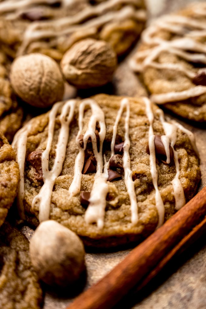 Spiced chocolate chip cookies on a surface with whole nutmeg and cinnamon sticks around it.
