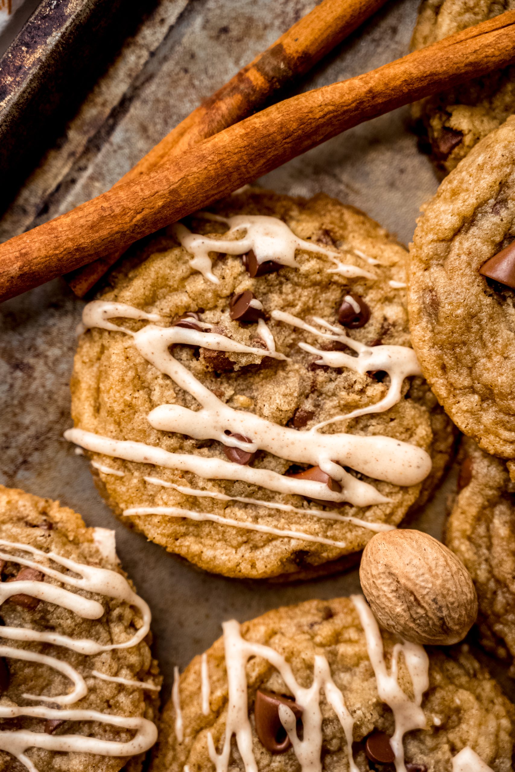 Aerial photo of spiced chocolate chip cookies on a surface with whole nutmeg and cinnamon sticks around it.
