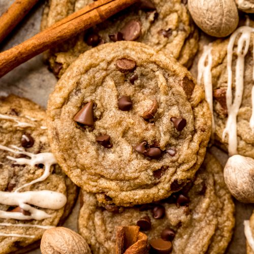 Aerial photo of spiced chocolate chip cookies on a surface with whole nutmeg and cinnamon sticks around it.