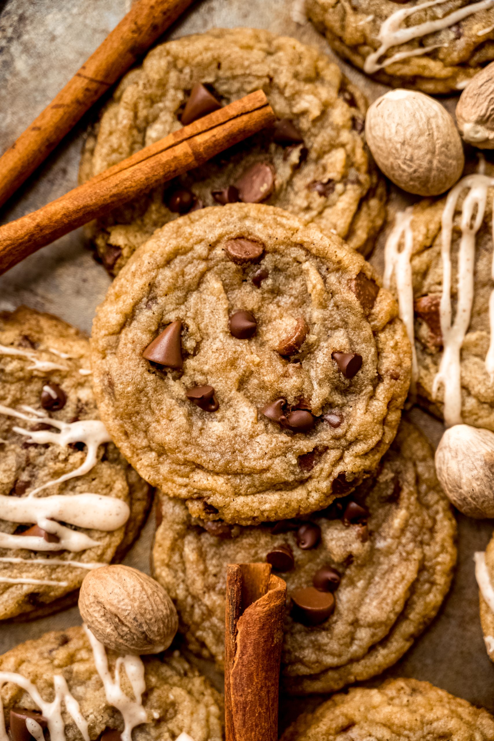 Aerial photo of spiced chocolate chip cookies on a surface with whole nutmeg and cinnamon sticks around it.